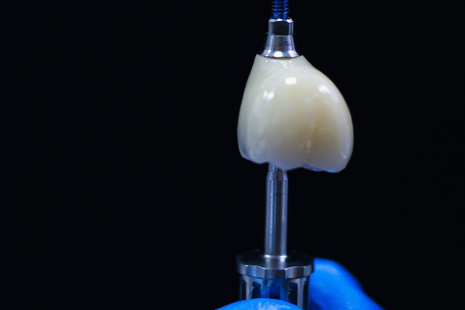Coroană dentară din ceramică, montată pe piesa de legătură a unui implant, ținută cu mănuși